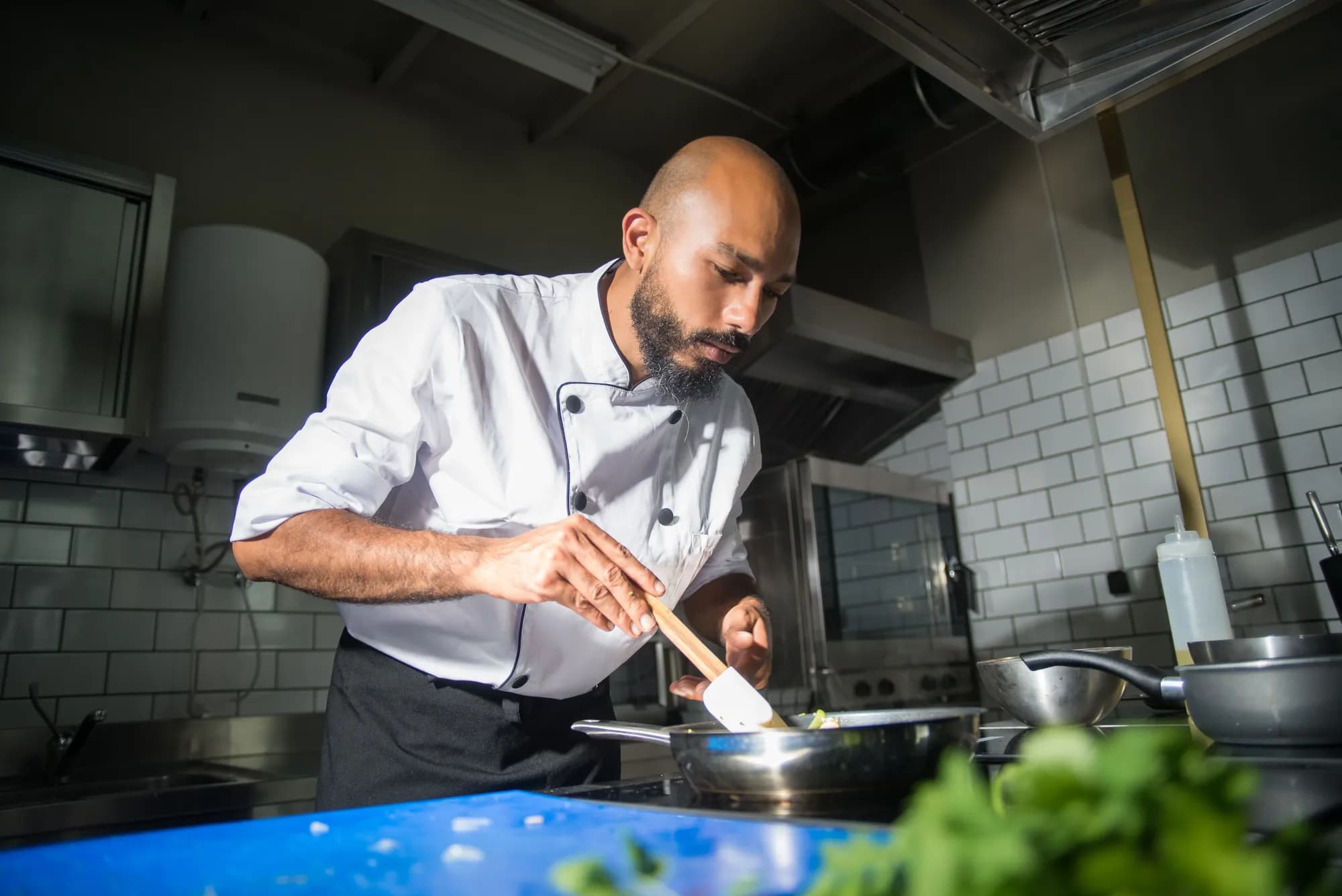 Cozinheiro de dólmã mexendo a panela no fogão de uma cozinha profissional clara
